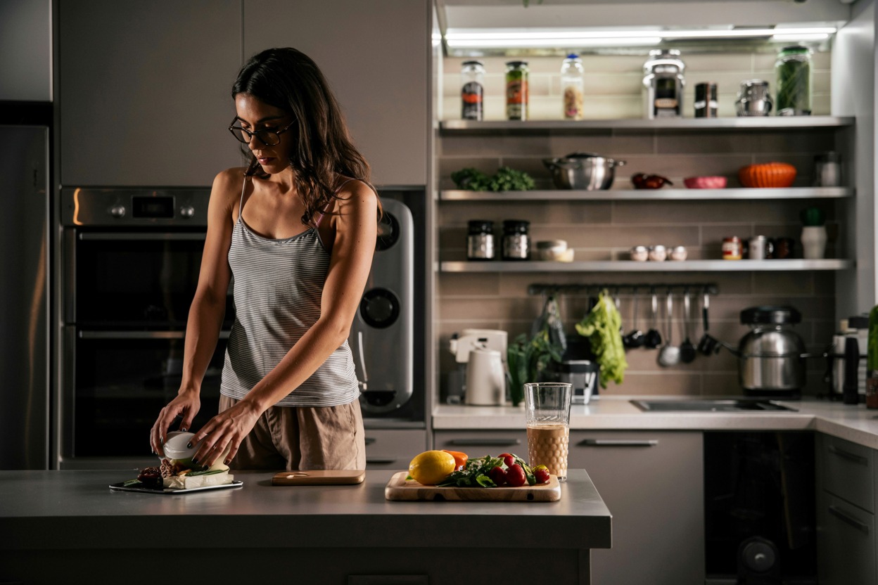 Devojka priprema obrok u modernoj kuhinji sa svežim povrćem i napitkom na radnoj površini- vegetarijanska ishrana u svakodnevnom životu.